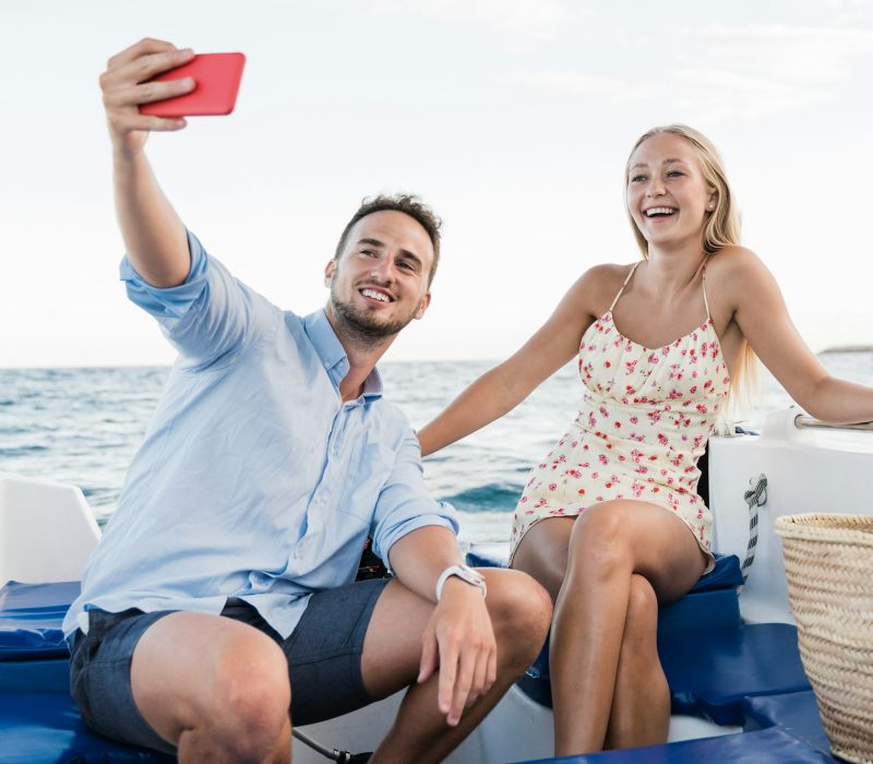 Happy young couple having fun on sailing boat taking selfie during luxury summer vacations